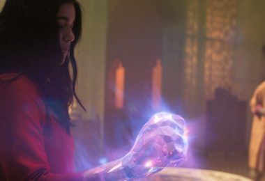 Kamala Khan, aka Ms. Marvel, is shown in profile as she displays her illuminated and enlarged fist to Waleed, a new character and mentor to the Red Daggers, who stands in the background in a darkened sanctuary.